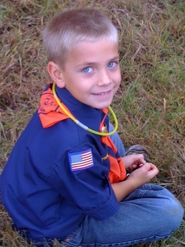 Cash as a kid in his Cub Scout uniform, sitting in the grass